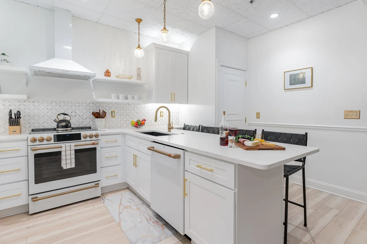 A stylish kitchen with a central island, modern stove, golden faucet, hanging lights, and shelves adorned with decorative items. The design is warm and welcoming, perfect for hosting meals or casual hangouts in either of the two units.
