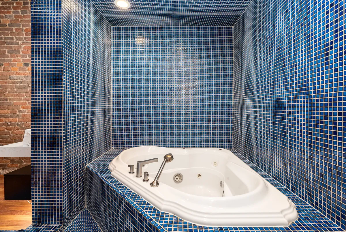 A tranquil bathroom scene with a large jacuzzi tub, blue mosaic tiles, and brick accents, creating a luxurious space for unwinding and self-care.