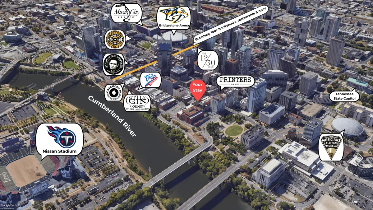 A wide-angle city view that includes the Cumberland River, Bridgestone Arena, Nissan Stadium, and the Tennessee State Capitol. The image highlights both the vibrancy of downtown Nashville and the close proximity of major entertainment venues and nightlife hotspots.