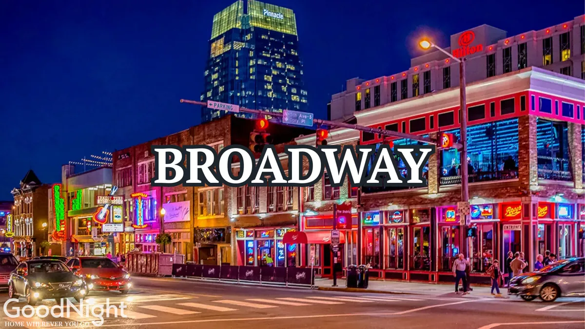 A lively nighttime scene along Nashville’s Broadway, featuring vibrant neon signs, bustling sidewalks, and a variety of storefronts that hint at the area’s famous honky-tonks and live music venues. The energetic crowd reflects the city’s reputation for nightlife and entertainment.