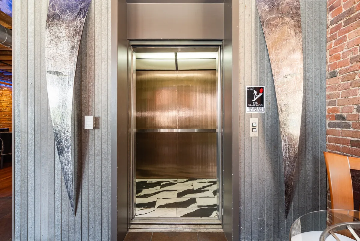 A contemporary entryway featuring a private elevator, metallic art, and a textured wall. The inviting space hints at seamless arrival and exclusive access, aligning with the narrative of arriving in style and the ease of in-and-out flow.